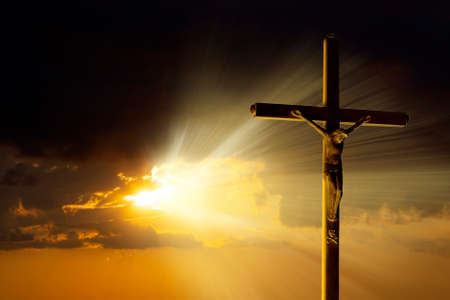 The crucifixion cross stands against the backdrop of an impressive golden sky with radiant rays penetrating through the cloudsの写真素材