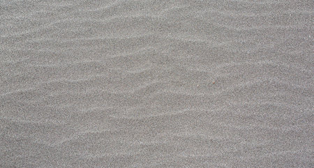 Wind is creating ripples on dark volcanic sand, providing a beautiful natural texture background