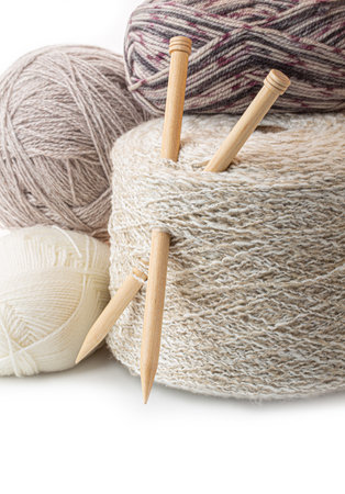 Wooden knitting needles are stuck into a textured skein of yarn, surrounded by other colorful yarn...