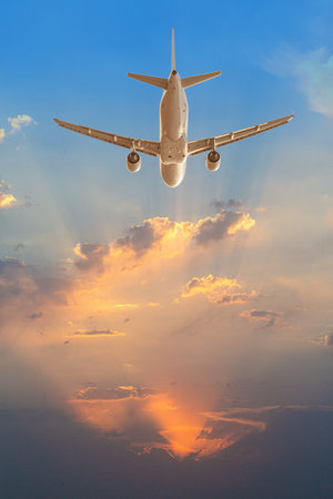 White passenger airplane flying high above orange clouds during sunset