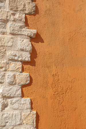 Rough stone bricks meet orange textured plaster wall creating abstract backgroundの写真素材