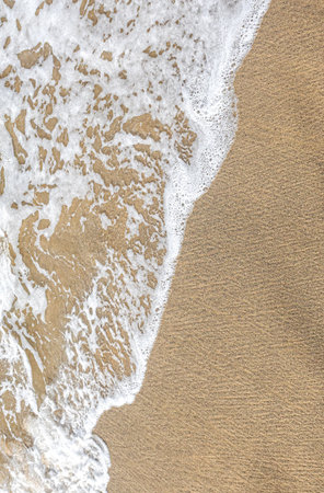 Foaming ocean water receding on textured sand, creating abstract patternsの写真素材
