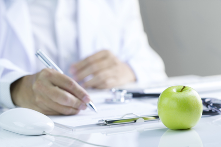 Green apple on glossy white desktop with doctor out of focus in white shirt in background in concept ofの写真素材