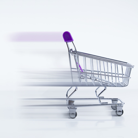 Shopping cart in motion blur effect showing fast delivery service concept. Presented on white background and glossy white floor.の写真素材