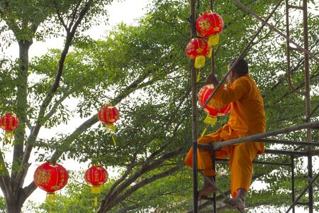 Nonthaburi, Thailand - 4 February 2018: Young Thai-Chinese buddhist monk on a scaffolding hanging red lanterns on the trees as a decoration accessory in preparation for the up-coming Chinese new yearのeditorial素材