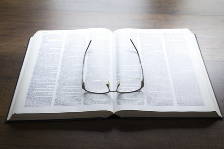 Black eyeglasses lying on an opened thick book isolated on black background in warm tone.