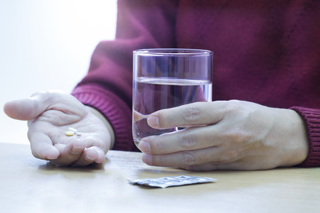 Hands holding pills and pure water showing action of taking some solid medicines.の写真素材