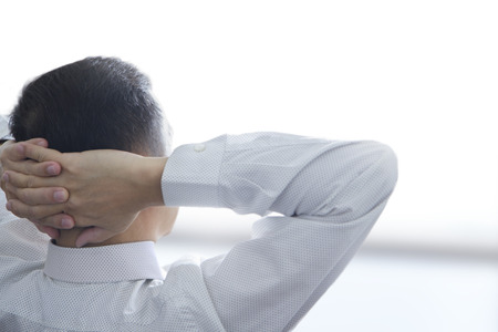 Rear view of businessman in white shirt in relaxing posture at the end of the day after a hard work...