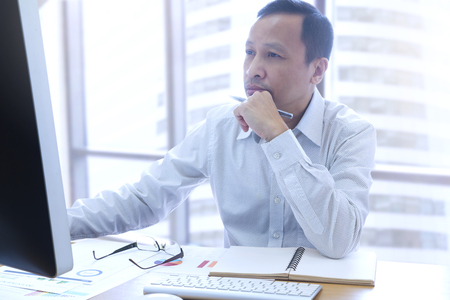 Businessman using a desktop computer analysing return on investment or finance and accounting information in the office with city backgroundの写真素材