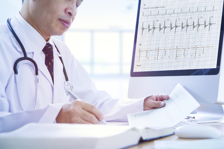 Asian doctor researches and analyses a patientâs health data on heartbeat graph in front of computer.の写真素材