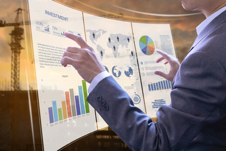 Businessman in front of modern virtual touch screen analysing on investment risk management and return on investment analysis on real estate building contruction.の写真素材
