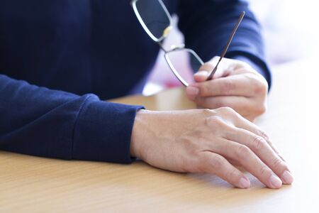 Closeup of a man in blue holding eye-glass in gesture of listening carefully with an intention during a conversation in which news and ideas are exchanged.の写真素材