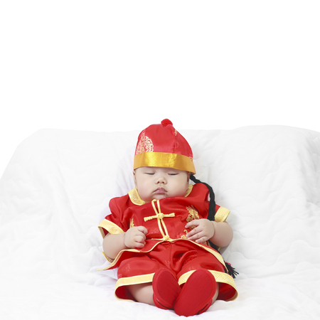 Asian baby boy wearing red Chinese suit or clothes with hat sit and sleeping lay drooling on white bed or sofa for Chinese New Year festiva in studio with copy spaceの写真素材