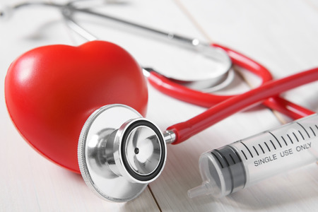 closeup red heart rubber with stethoscope medical instrument and syringe on vintage white wood table for love memorial or take care and treat heart disease for strength of health with spaceの写真素材