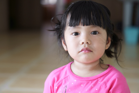 closeup Asian children cute or kid girl and big eye with look at the face and displeased or frown angry at home with spaceの写真素材
