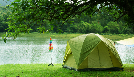 nature landscape green camping tent with colorful umbrella under the tree and blue with yellow tarp on meadow with lake or river and tree mountain for holiday relax on winter and gray sky at ched khotの写真素材