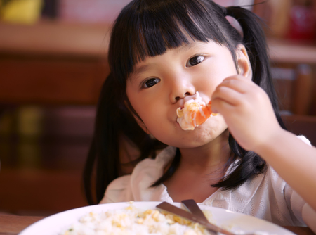 Asian children cute or kid girl eating shrimp or shrimp fried rice delicious food on table and white dish for lunch in the restaurantの写真素材