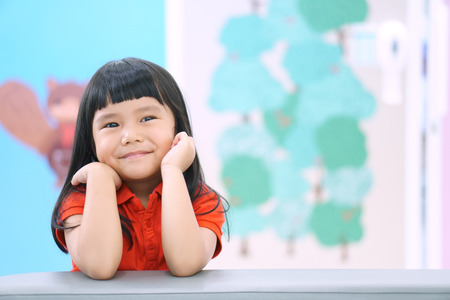 Asian children cute or kid girl think and happy fun or smile with wear red shirt on sofa at preschool or nursery and child hospital with spaceの写真素材