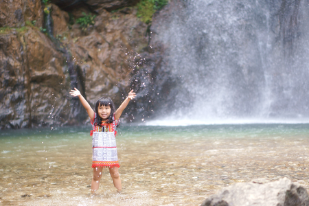 Asian children cute or kid girl smile with fun and enjoy playing water splash on waterfall and holiday relax trip for summer at Jokkradin waterfallの写真素材