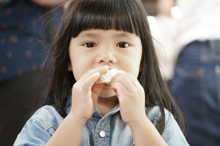 Asian cute children or kid girl and long hair eating bread for dessert or snack and wearing jeansの写真素材