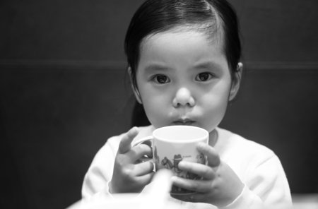 Asian children cute or kid girl drinking water in white cup at cafe restaurant and looking on dark black and white style for memorialの写真素材