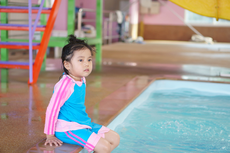 Asian children cute or kid girl sitting by the swimming pool and smile with happy fun in water park for refreshing and relax with exercise on summer holiday with spaceの写真素材