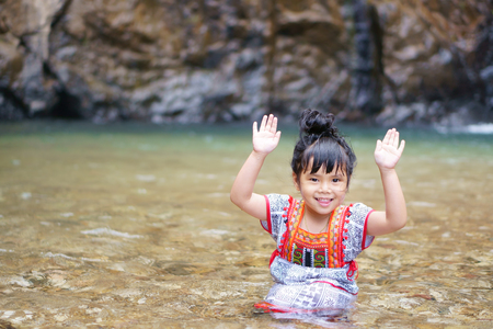 Asian children cute or kid girl and hill tribe smile with fun and enjoy playing water splash with hands up on waterfall or river and holiday relax trip for summer at Jokkradin waterfallの写真素材