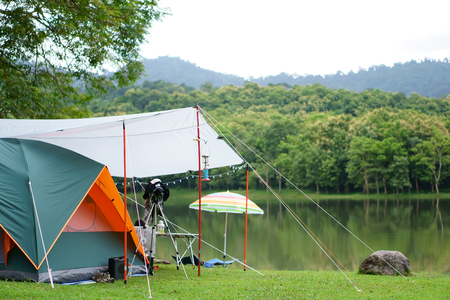 nature orange with green camping tent and gray fly sheet with tent accessory on meadow with lake or river and tree mountain for holiday relax on rainy season and white sky at ched khotの写真素材