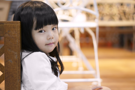 Asian children cute or kid girl sit lean on wood balcony for relax with eye looking camera and little smile in home with spaceの写真素材