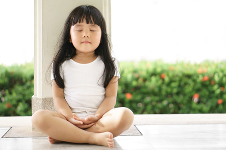 Asian children cute or kid girl sit for meditation with peace and relax in garden pavilion at temple or church and wearing white dress with sunlight on white with spaceの写真素材