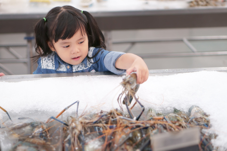 Asian children cute or kid girl holding and choose fresh shrimp in ice tray for seafood sales or buy and shopping at supermarketの写真素材