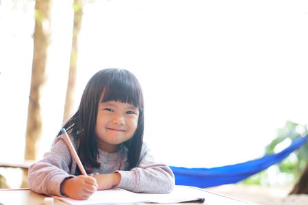 Asian children cute or kid girl fun with smile and learning for coloring or paint and writing on white paper or book at nursery or school on nature with white spaceの写真素材