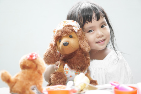 Asian children cute or kid girl smile with fun and enjoy playing dog doll for relax and learning at nursery home on soft focusの写真素材