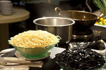 yellow spaghetti and spaghetti squid ink or spaghetti con li seppie nero with steam on hot water stainless pot and brass pan on stove for prepare italian food in restaurant or hotel on warm whiteの写真素材