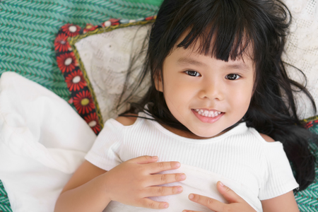 Asian children cute or kid girl open eye sleeping on green mat with white blanket and pillow with smile and beautiful face with teeth on bedtime in bedroom at home with spaceの写真素材