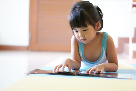 asian children cute or kid girl lie down with learning and reading a book or story on the floor at home for educationの写真素材