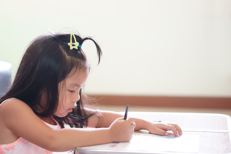 asian children cute or kid girl diligent review and enjoy doing homework or happy learning and training write on white paper or book at nursery or school and kindergarten on table in room or classroomの写真素材