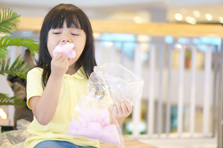 asian children cute or kid girl fun and smile with enjoy eating pink candy floss or cotton candy delicious for sweet sugar dessert and relax in department storeの写真素材