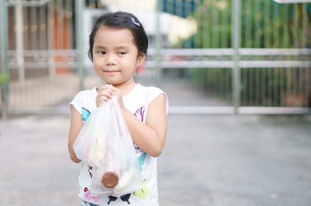Asian children cute or kid girl smile and holding plastic bag from shopping or buy food and snack or dessert at fresh market for breakfast or lunch on holidayの写真素材
