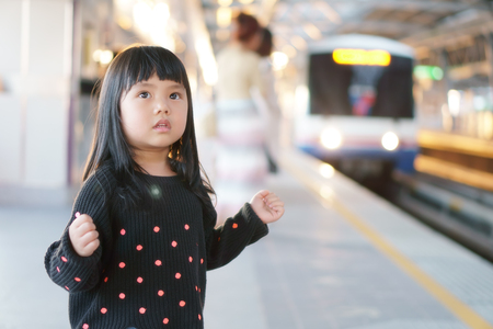 Asian children cute or kid girl waiting sky train or electric train on railway station or platform and nature sunlight in the city for travel and transportation with spaceの写真素材