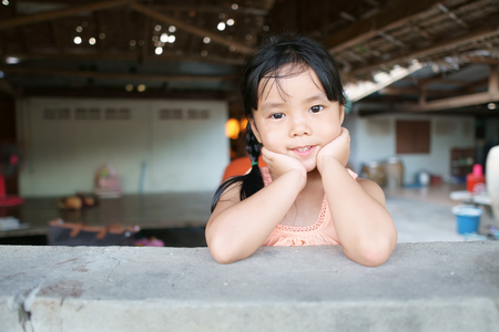 Asian children cute or kid girl and country child poor with hand to cheek and smile wear traditional top or sleeveless shirt at countryside old wooden home and terraceの写真素材