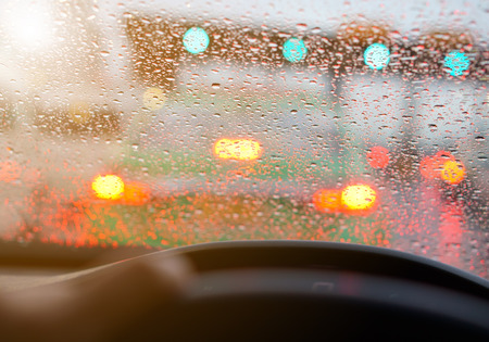 people driving car and water droplet on car mirror or windshield with rain or storm and traffic jam on expressway road although the green light with warm sunlightの写真素材