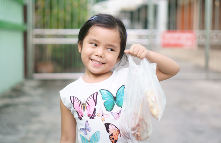 Asian children cute or kid girl smile and holding plastic bag from shopping or buy food and snack or dessert at fresh market for breakfast or lunch on holidayの写真素材