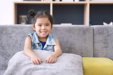 Asian child or kid girl and student thinking for new idea and happy fun or smiling white teeth with sit on sofa at kindergarten classroom or nursery and children dental hospital or home schoolの写真素材