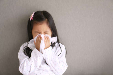 Asian child or kid girl sick with sneezing on nose and cold cough on tissue paper because weak or virus and bacteria from dust weather and kindergarten and pre school for medical background gray spaceの写真素材