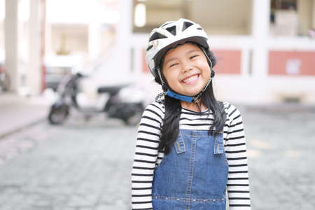 Asian child cute or kid girl wear white motorcycle or bike helmet with happy smiling white teeth for confident and head safety or sport exercise protect on street and road riding or driver travelの写真素材