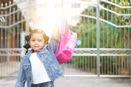 Asian child or kid girl smiling and student holding and show schoolbag in morning for committed determine with happy on go to school or back to school and kindergarten on summer study or home learningの写真素材