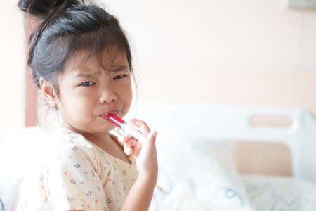 Asian child or kid girl Influenza A sick and eating or taking red drug or water medicine by syringe pump and make face bitter on bed at hospital room for pediatric patient treatment and healthcareの写真素材