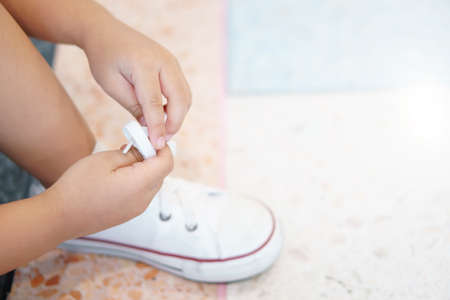 hand and foot of child or kid girl learning and try tie shoelace on white shoe or sneakers rope and footwear for keep walking or travel walk and fashion on street with independent and freeの写真素材