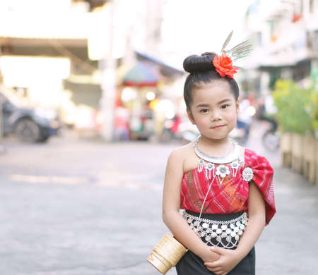 asian child cute or kid girl smiling with happy and wear red traditional thai dress or costume beautiful with rice wicker basket for thai seang retro style on fashion festival in thailand on streetの写真素材